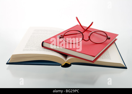 red and blue books with reading glasses on a reflecting white background - horizontal Stock Photo