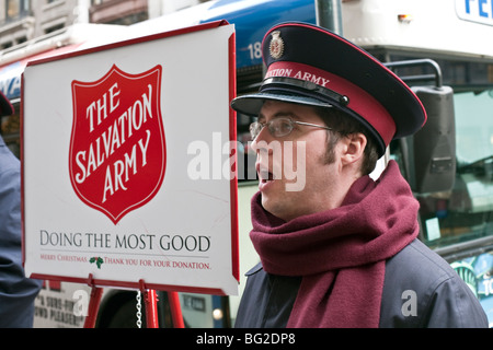 serious young Salvation Army officer wearing warm muffler singing Christmas carols for donations on Fifth Avenue New York City Stock Photo