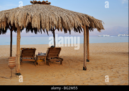 Relaxation on beach by sea under thatched sunshade, Nuweiba, 'Red Sea', Sinai, Egypt Stock Photo