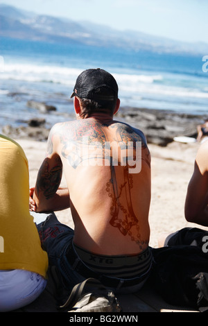 Man with cross tatooed on back watching surf competition in Spain Stock Photo