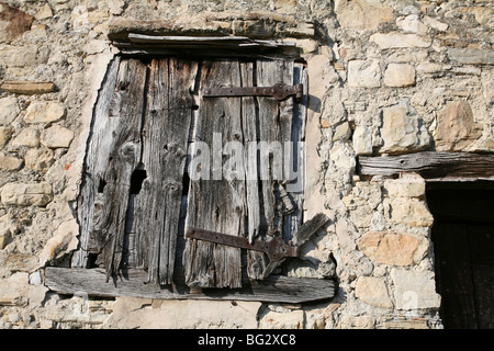 Very old and weathered wooden window shutter, rustic old stone walled house, in full sun. Stock Photo