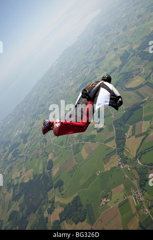 Skydiver within a special wingsuit is flying over a nice land scape scenery. The Birdman is going fast forward in the sky. Stock Photo