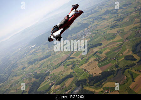 Skydiver within a special wingsuit is flying over a nice land scape scenery. The Birdman is going fast forward in the sky. Stock Photo