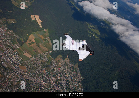 Skydiver within a special wingsuit is flying along a cloud edge over nice land scape scenery. The Birdman is going fast forward. Stock Photo