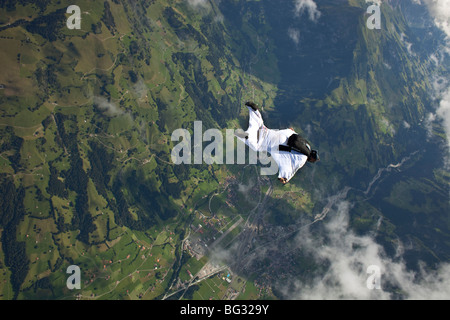 Skydiver within a special wingsuit is flying along a cloud edge over nice land scape scenery. The Birdman is going fast forward. Stock Photo