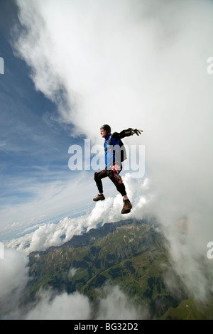 Skydiver is flying head up within the sit fly position in front of a big cloud scenery with over 120 MpH speed. Stock Photo