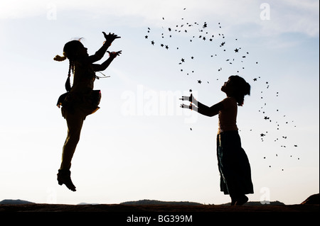 Silhouette of two young Indian girls jumping, throwing and catching stars. India Stock Photo