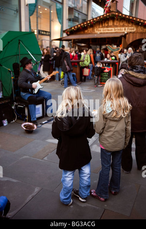UK, England, Manchester, Market Street, two young girls watching blues guitar playing busker Stock Photo