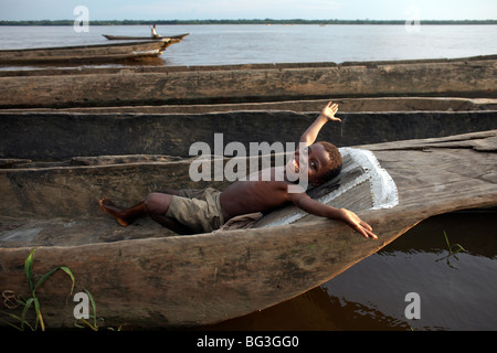 A boy relaxes in a dugout canoe on the Congo River, Yangambi, Democratic Republic of Congo, Africa Stock Photo