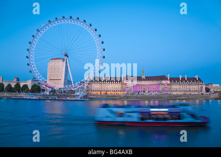 England, London, Westminster, Tourist boat passes infront of The London Eye and County Hall at night Stock Photo
