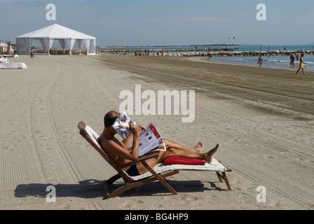 Italian holidaymaker, lone male on the beach, using a folded newspaper as a sunshield, shading his face.Venice Lido Italy 2000s. Stock Photo