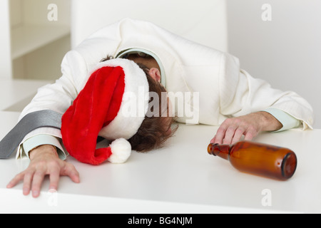 Strongly drunk man in a Christmas cap lies on a table at office Stock Photo