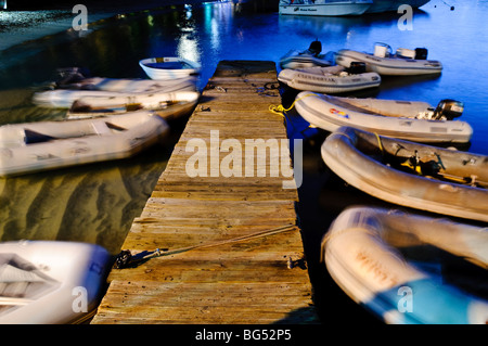 Jetty Dinghies Cruz Bay St John US Virgin Islands | ST JOHN, US Virgin Islands — A wooden jetty at Cruz Bay harbor is lined with dinghies rendered as motion blurs during a long-exposure dusk photograph, a technique that captures the gentle rocking of small boats moored for the night. Dinghies like these ferry passengers between shore and the sailboats and yachts anchored in the bay. Stock Photo