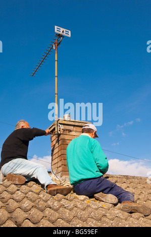 Two builders re-pointing a chimney (raking out the cement joints and renewing the cement) in the Uk Stock Photo