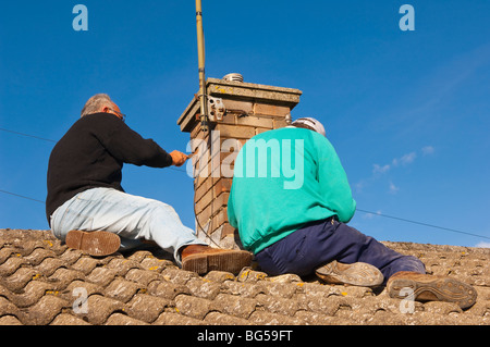 Two builders re-pointing a chimney (raking out the cement joints and renewing the cement) in the Uk Stock Photo
