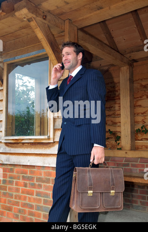 Businessman in his late twenties standing at a rural bus stop talking on his mobile phone Stock Photo