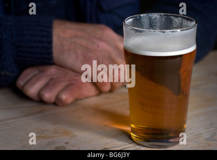 pint of bitter with mans hands behind resting on scrubbed wooden table Stock Photo