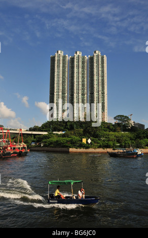 Portrait shot of a small boat taxi, moving westwards past three high rise buildings, Aberdeen Harbour, Hong Kong, China Stock Photo