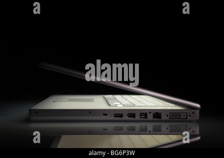 Silver laptop laptop with a luminous screen on a reflection surface, on a black background with copy space. Side view. Stock Photo