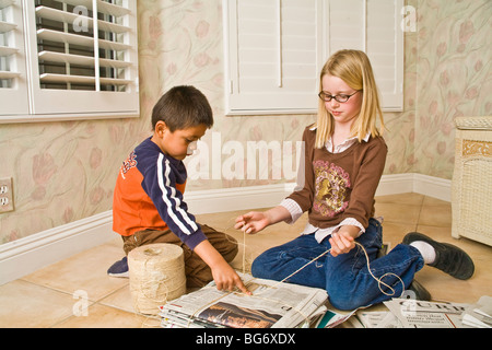 Hispanic boy 5-6 and Caucasian girl 8-10 year old work together to bundle newspapers for recycling help children child helping another service MR  © Myrleen Pearson Stock Photo