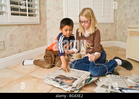 Hispanic boy 5-6 Caucasian girl 8-10 year old work together bundle newspapers recycling help older younger children child helping another  © Myrleen Pearson Stock Photo