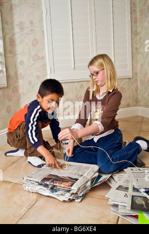 Hispanic boy 5-6 and Caucasian girl 8-10 year old work together to bundle newspapers for recycling help children child helping another service MR  © Myrleen Pearson Stock Photo