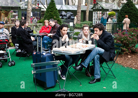 people at outdoor tables among Christmas shops in Bryant park NYC include a tourist trio feasting on pizza & ignoring December Stock Photo