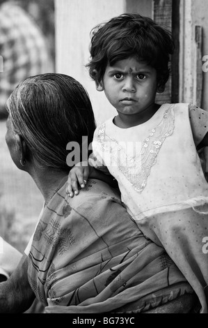 Indian toddler leaning on her grandmother in the doorway of there house in a rural indian village. Andhra Pradesh, India. Monochrome Stock Photo