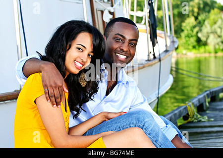 Young romantic couple sitting on dock in front of yacht Stock Photo