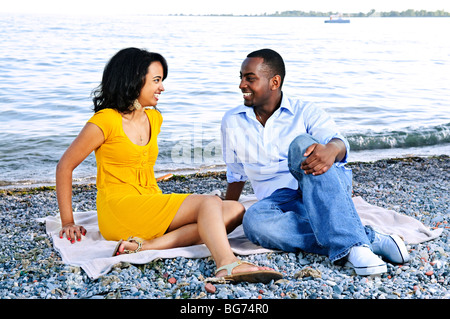 Young romantic couple looking at each other sitting on beach Stock Photo