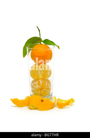 Whole peeled and unpeeled oranges stacked on one another within a glass tumbler. Stock Photo