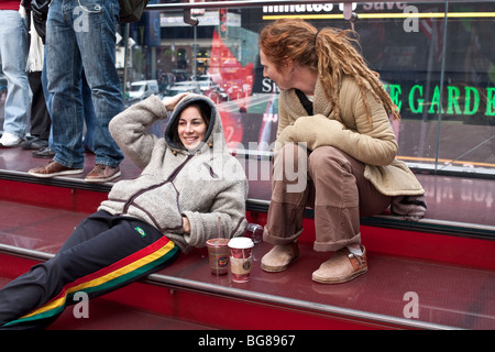 young woman with bright henna hair relaxes with her girlfriend on the viewing bleachers in the Times Square pedestrian mall NYC Stock Photo