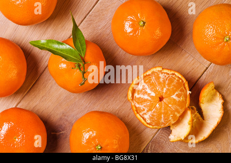 Overhead view of clementine fruits, one with leaves and one half peeled Stock Photo