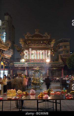 Lungshan (Longshan) Temple of Manka (Monga/Bangka/Mengjia) worshippers, food and flower offerings seen at night, Wanhua District, Taipei City, Taiwan Stock Photo