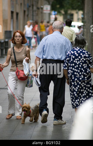 OLD PEOPLE, OUT WALKING, PET: A couple arm-in-arm pass an old woman with red hair and a dog on a backstreet Barcelona Catalonia Spain Stock Photo