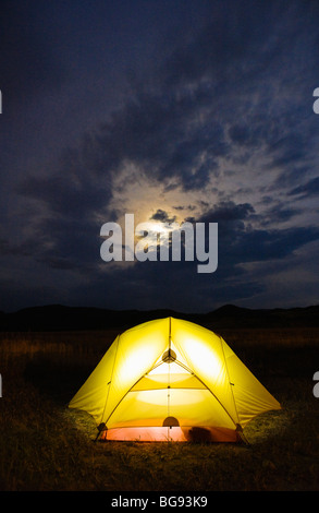A tent glowing from a light within with a cloudy moonrise above. Montana, USA. Stock Photo