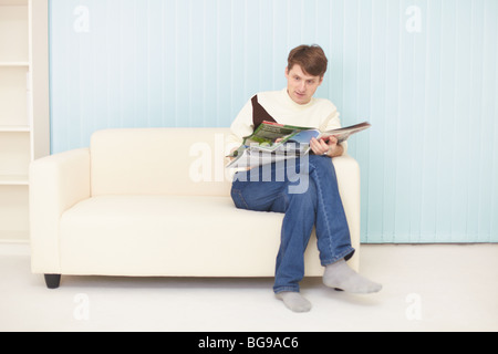The young man sits on a sofa with the journal Stock Photo