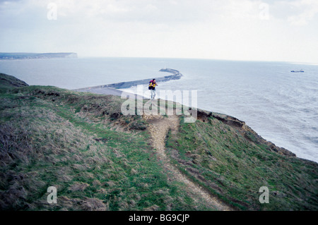 Hill walker walking along a cliff top path by the sea Stock Photo
