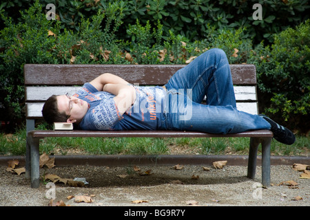 SLEEPING MAN, BOOK AS A PILLOW, BARCELONA: A man asleep during siesta with book as pillow on a park bench Barcelona Spain Stock Photo