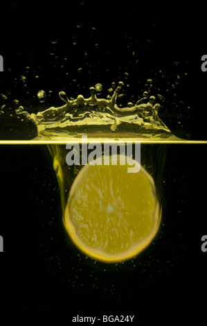 The lemon segment falls in water and creates round itself splashes against a dark background Stock Photo