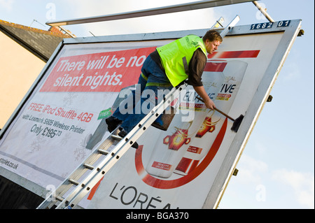 Worker up ladder with long handled brush pasting advertising poster on billboard site in Newport South Wales UK Stock Photo