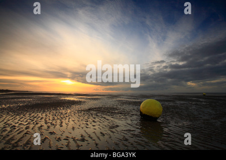 A yellow buoy on Heacham beach at sunset with a low tide on the Norfolk coast. Stock Photo