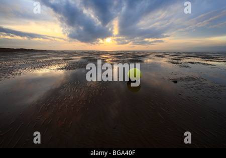 A yellow buoy on Heacham beach at sunset with a low tide on the Norfolk coast. Stock Photo