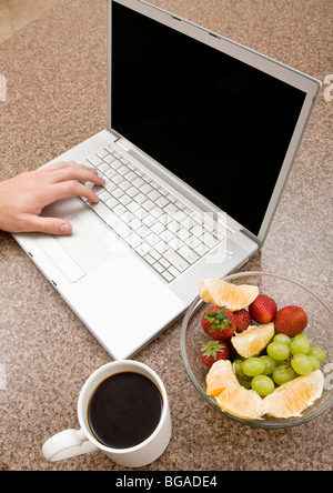 With a morning cup of coffee, a young person checks email and works on a laptop. Stock Photo