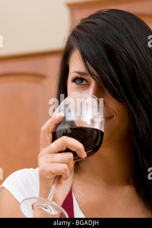 A young woman enjoys a glass of red wine at home in her kitchen. Stock Photo