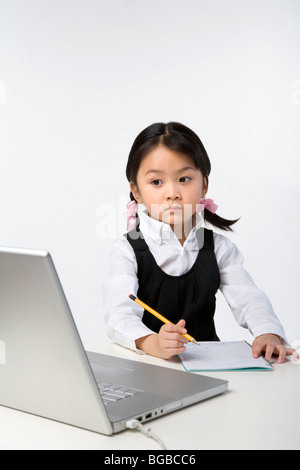 Little girl uses a laptop and a notebook Stock Photo