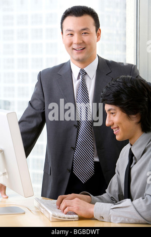 Man in business suit shows young employee something on a computer. Stock Photo