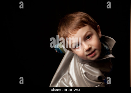 four to five year old boy looking at camera while twisting against a black background.