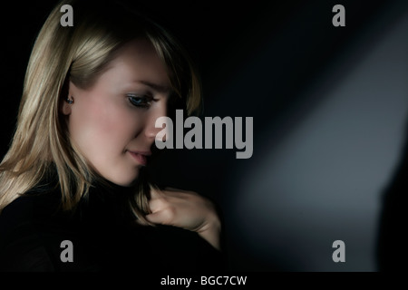 Side portrait of a young woman, surrounded by shadows, looking down Stock Photo