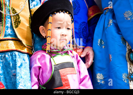 A young Mongolian child in traditional clothing flanked by three women whose faces cannot be seen Stock Photo